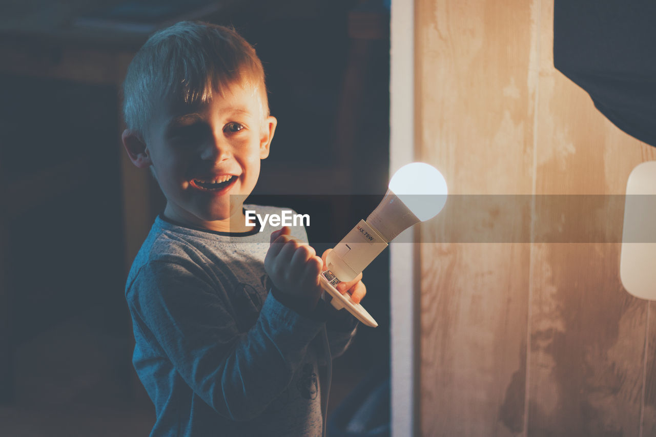 Smiling boy holding illuminated light bulb