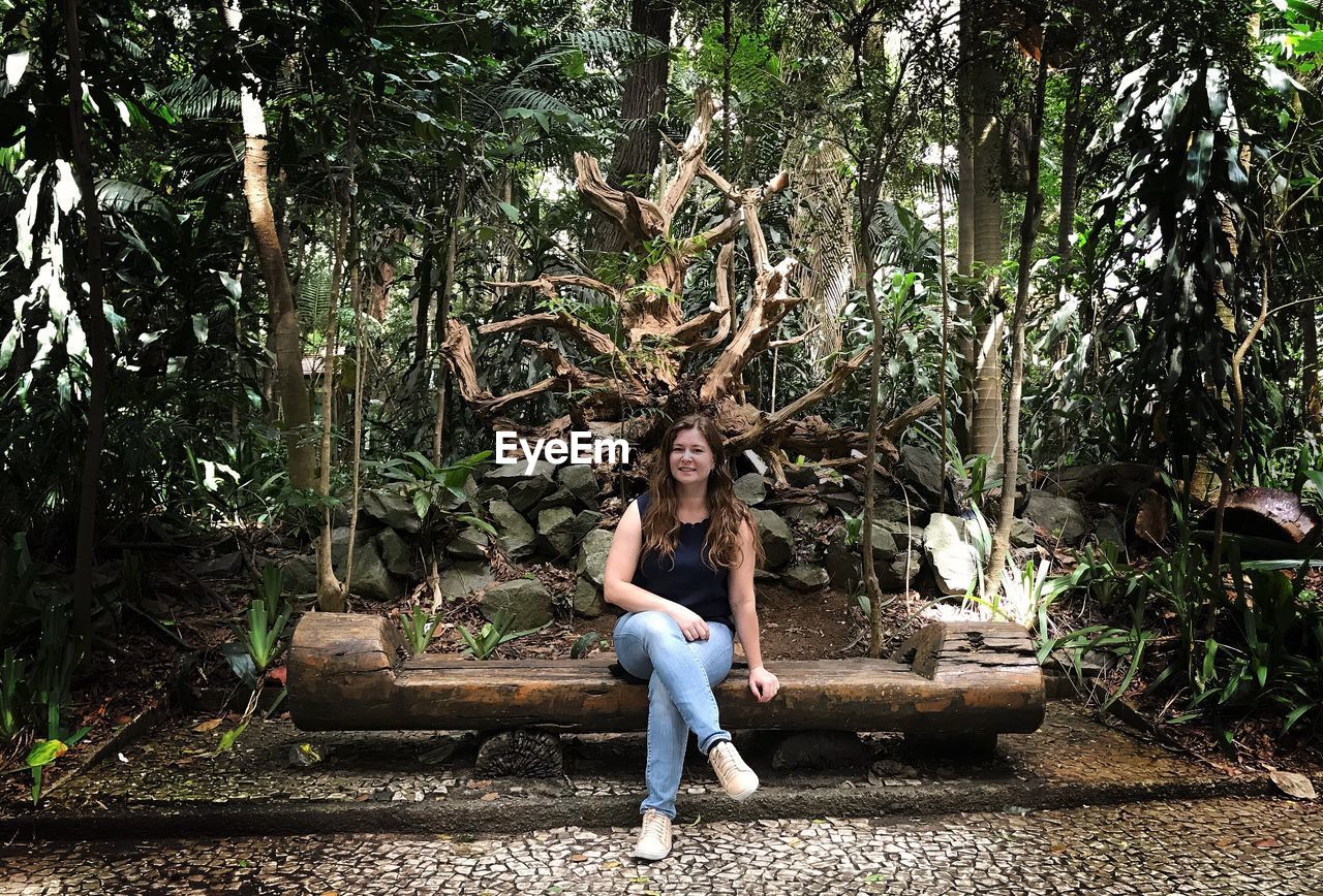 Portrait of woman sitting on seat in forest