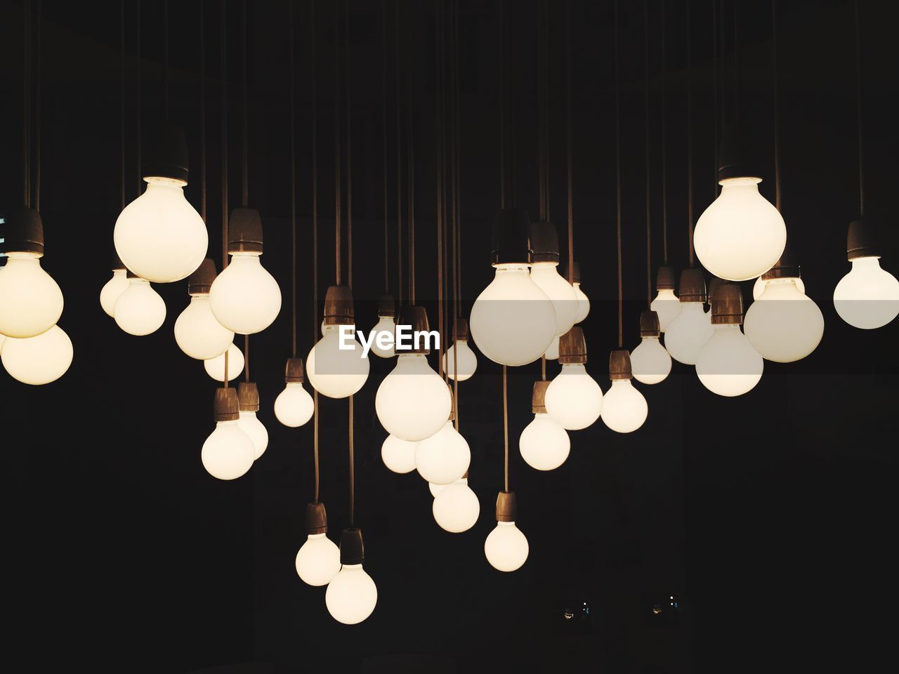 Illuminated light bulbs hanging against black background