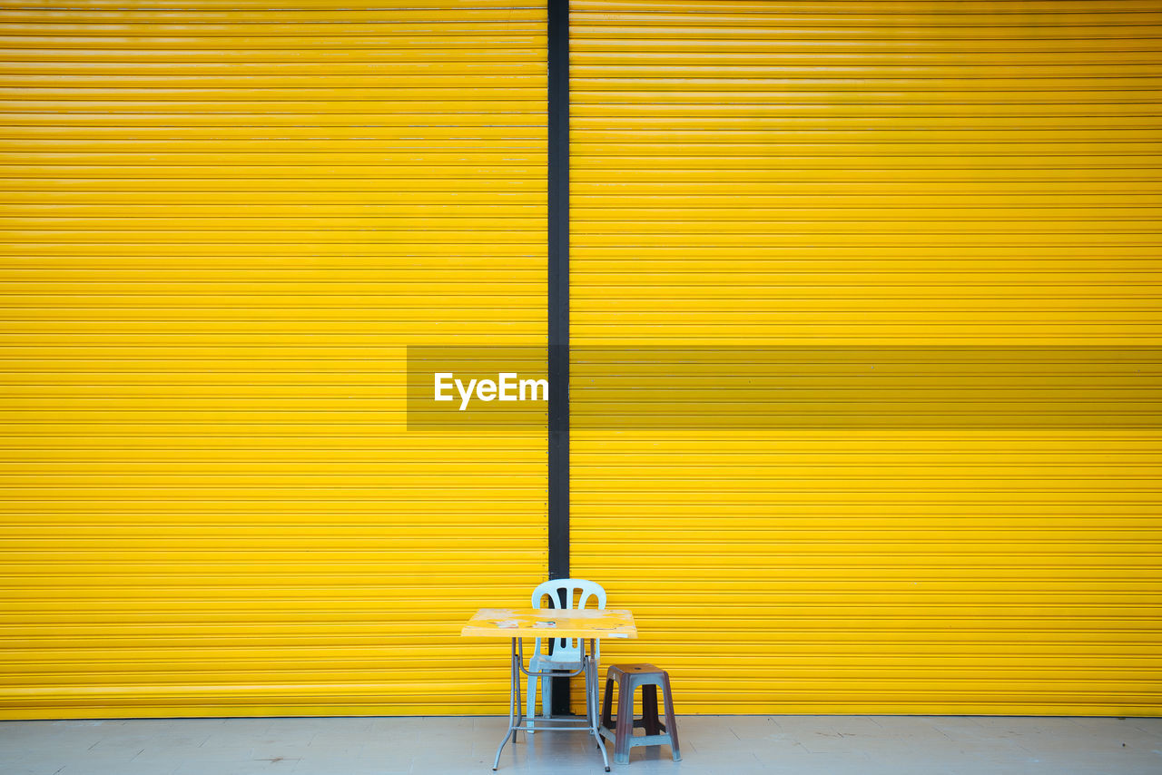 Chair and table against yellow closed shutter