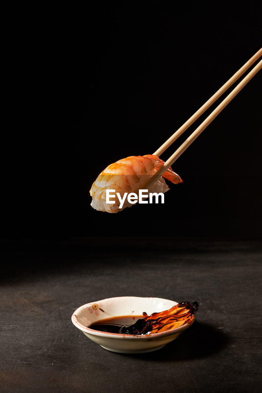 Shrimp sushi with chopsticks over dark background