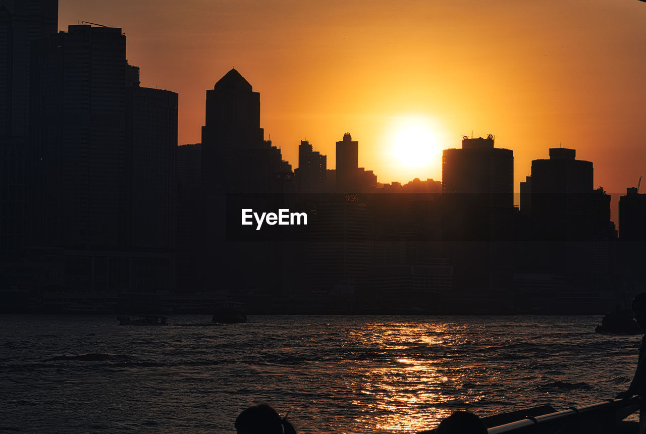 SILHOUETTE BUILDINGS BY SEA AGAINST SKY AT SUNSET