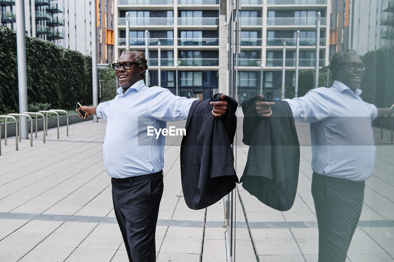 Carefree businessman with arms outstretched standing by glass wall