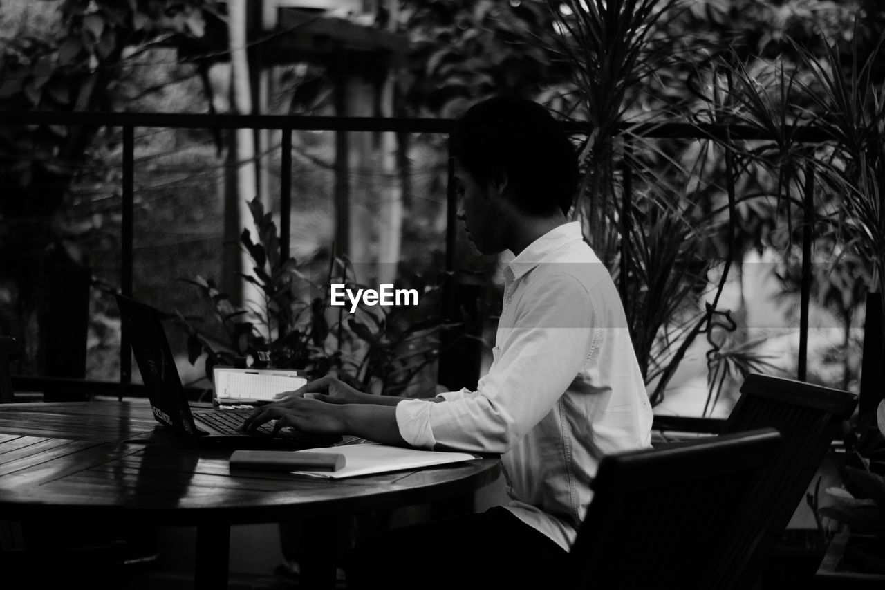 Side view of young man using laptop while sitting at table