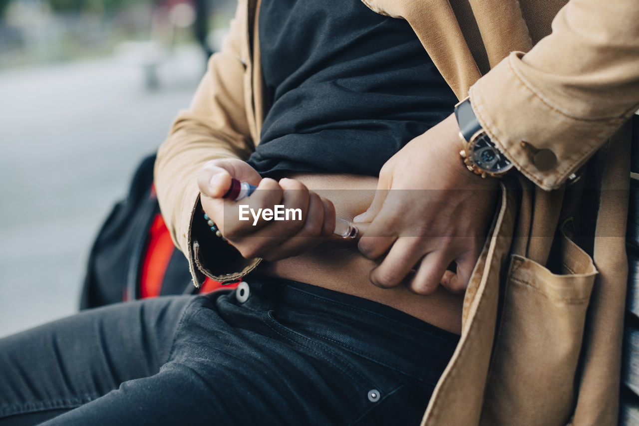 Midsection of man injecting insulin while sitting on bench