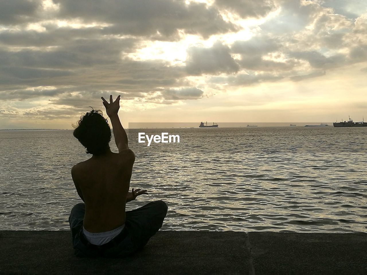 WOMAN SITTING ON BEACH AGAINST SEA DURING SUNSET