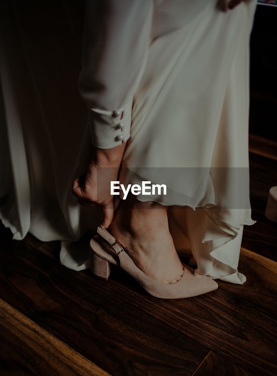 Low section of bride wearing heels on wooden floor