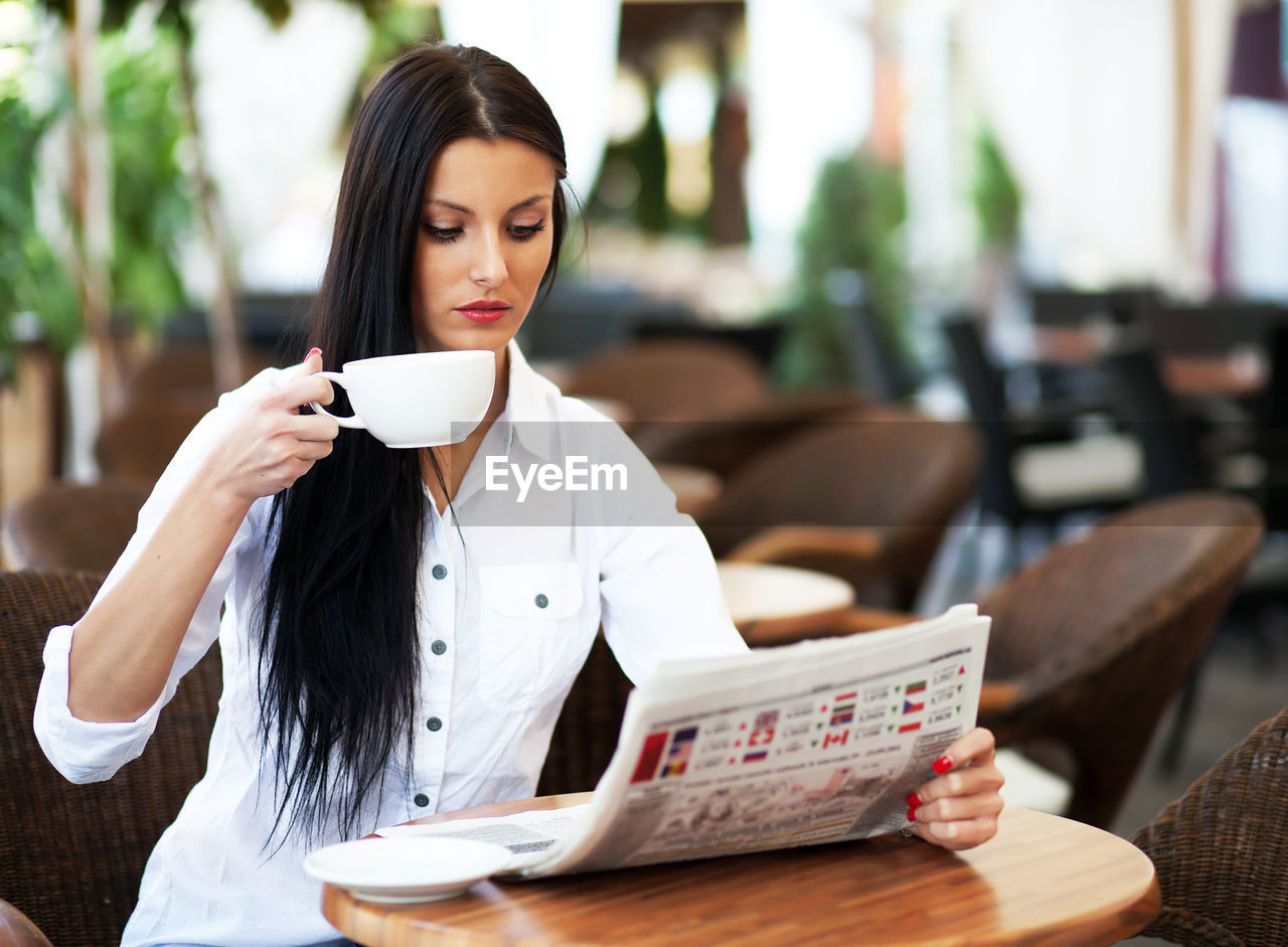 YOUNG WOMAN DRINKING COFFEE IN RESTAURANT