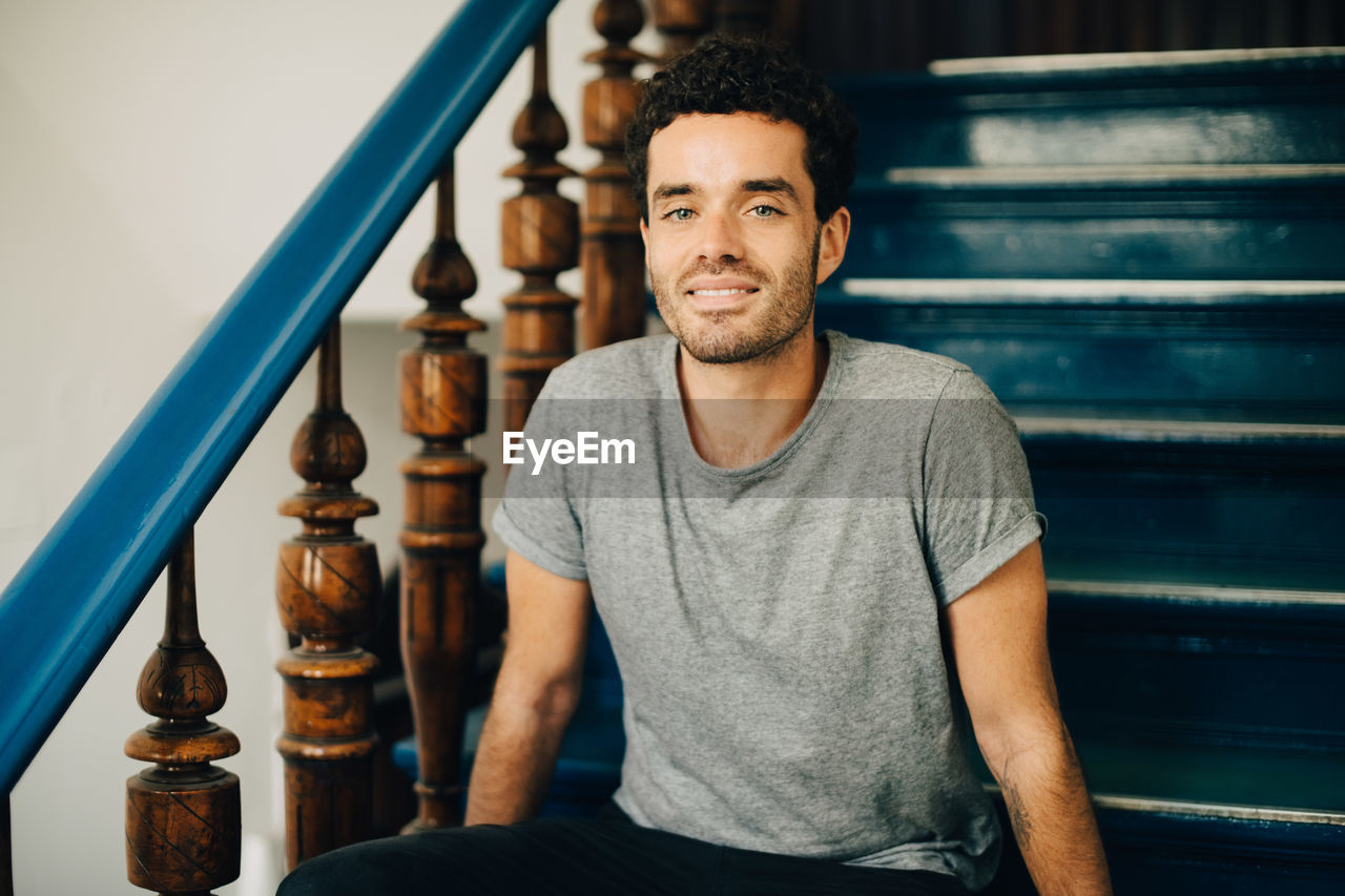 Portrait of smiling mid adult man sitting on steps in apartment