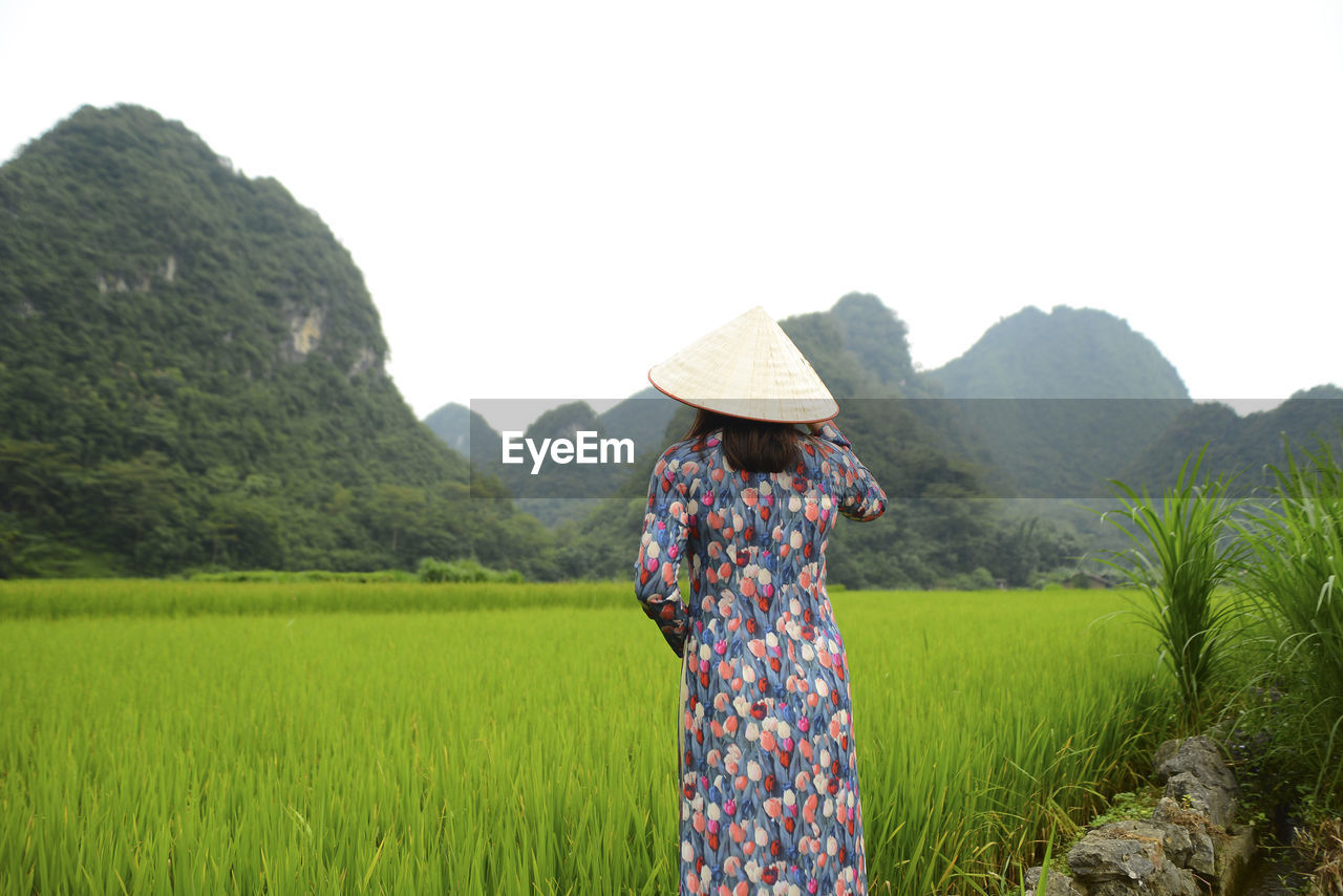 REAR VIEW OF PERSON WEARING HAT ON FIELD