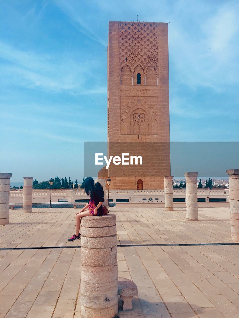 REAR VIEW OF WOMAN SITTING OUTSIDE BUILDING