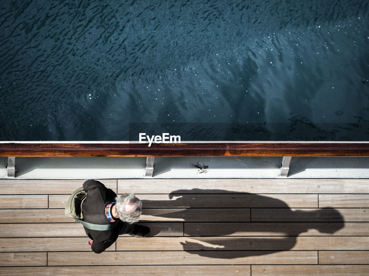 HIGH ANGLE VIEW OF MAN SITTING ON RAILING AT SHORE