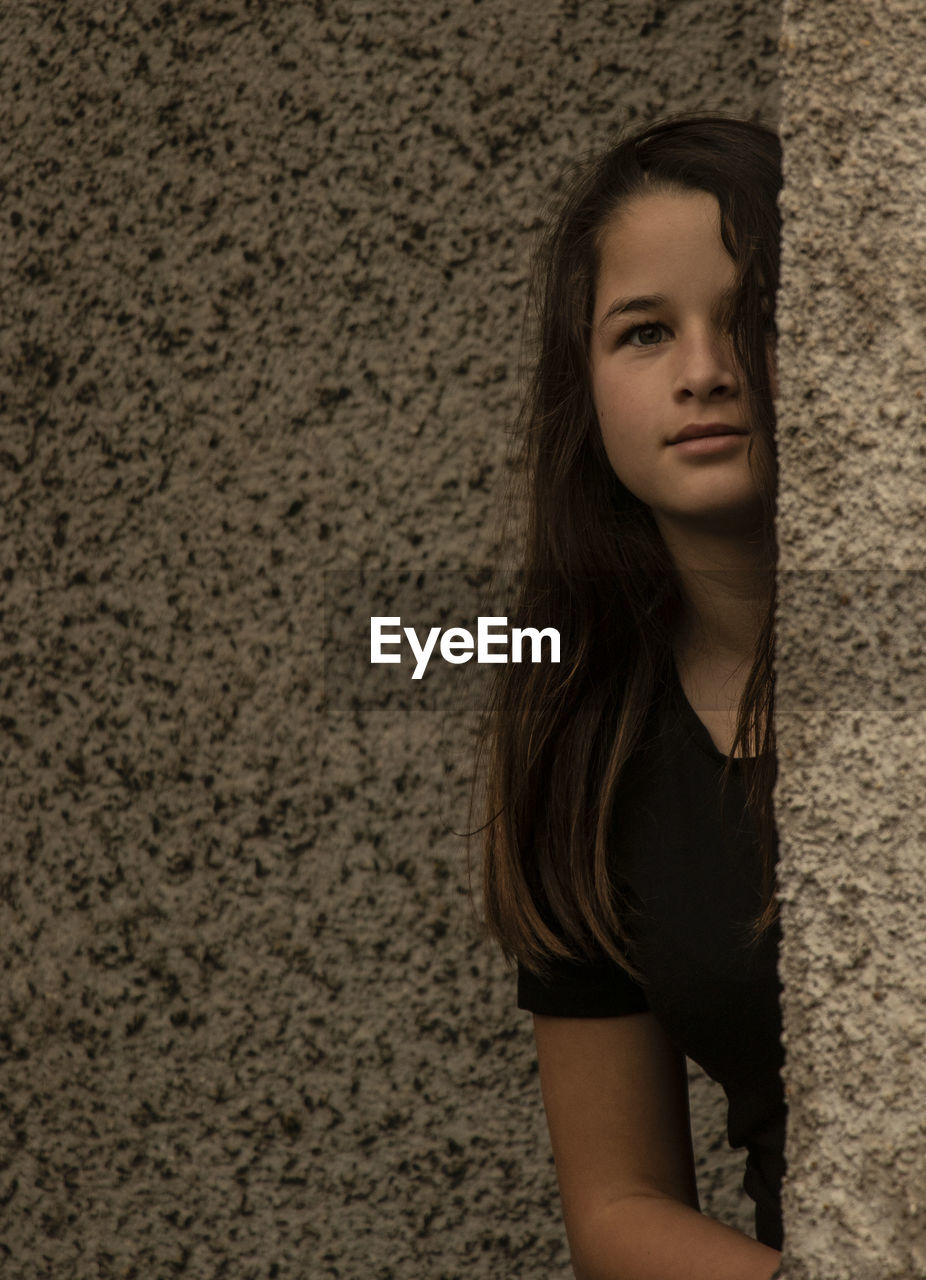 Portrait of girl hiding behind wall