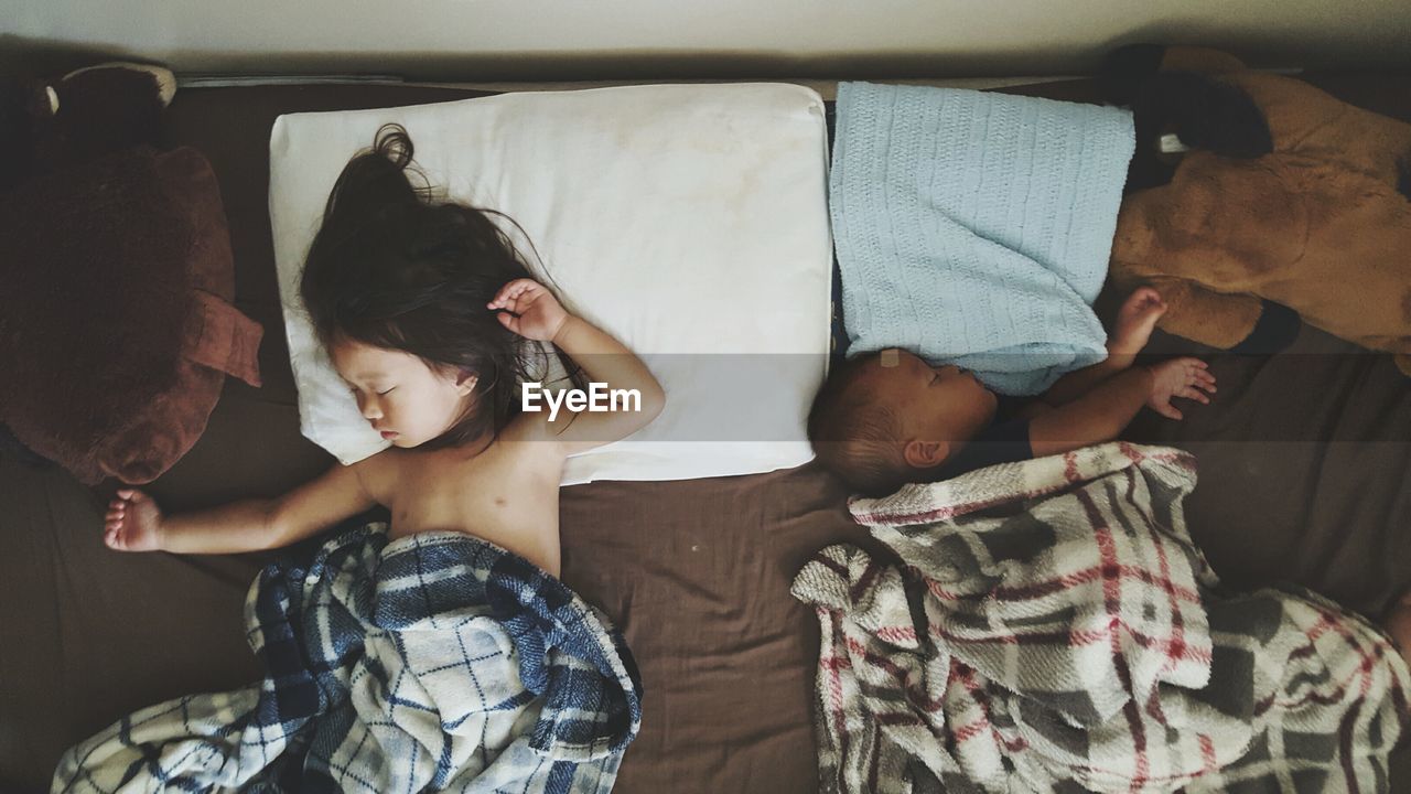 High angle view of siblings sleeping on bed at home