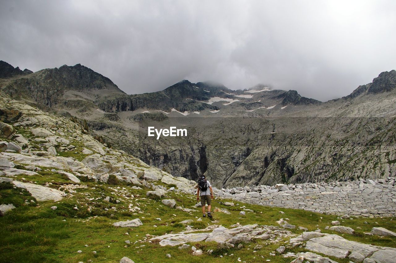 Man hiking on mountain against cloudy sky