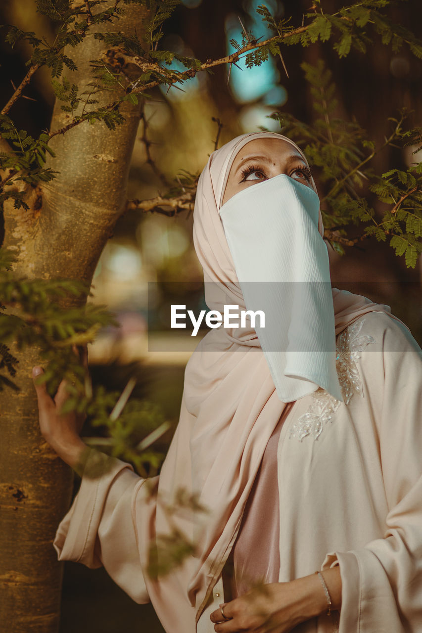 Portrait of veiled woman with white niqab and hijab standing against the tree