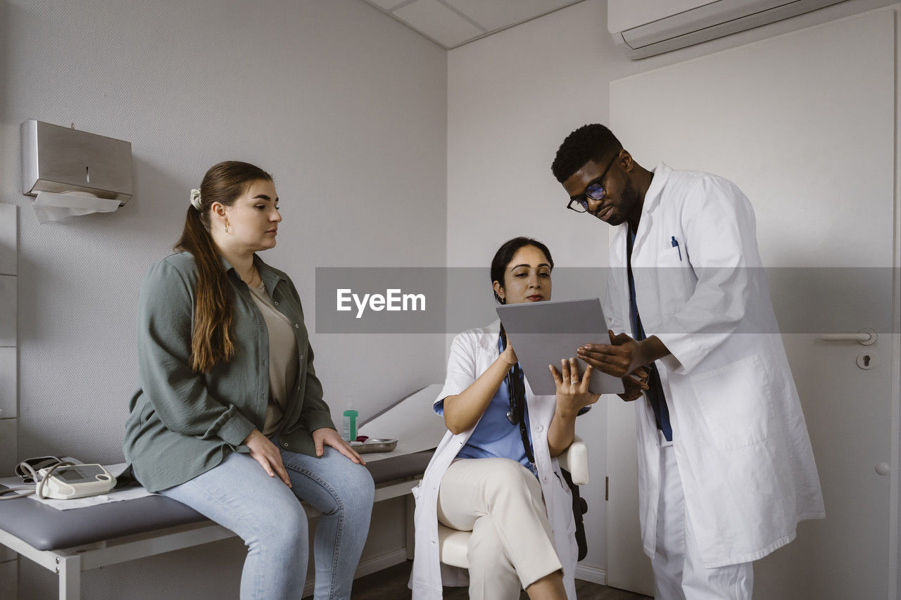 Male and female healthcare workers discussing over tablet pc with female patient in clinic