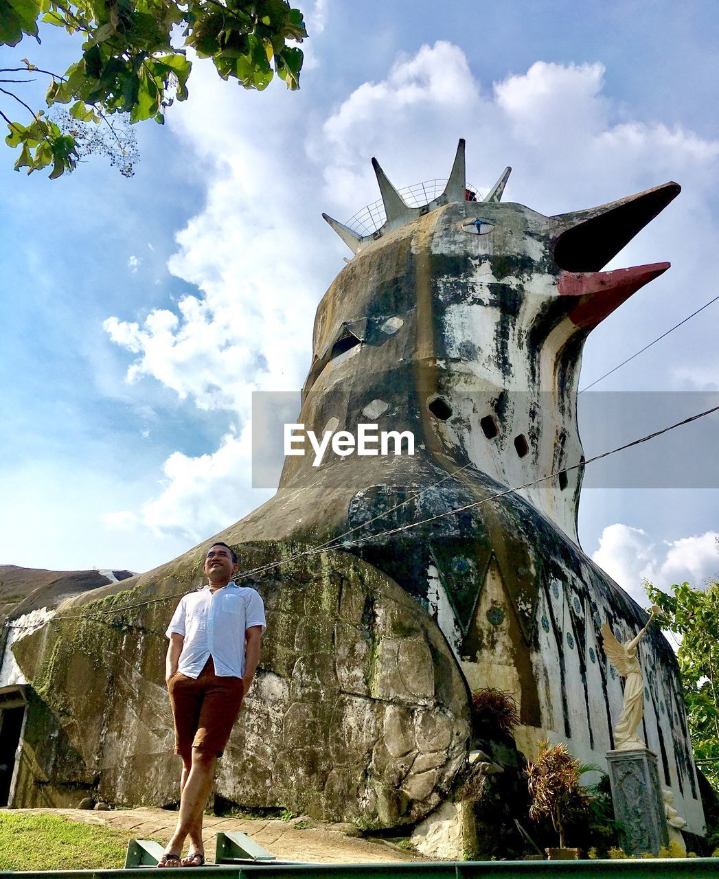 Low angle view of mature man standing by sculpture against sky