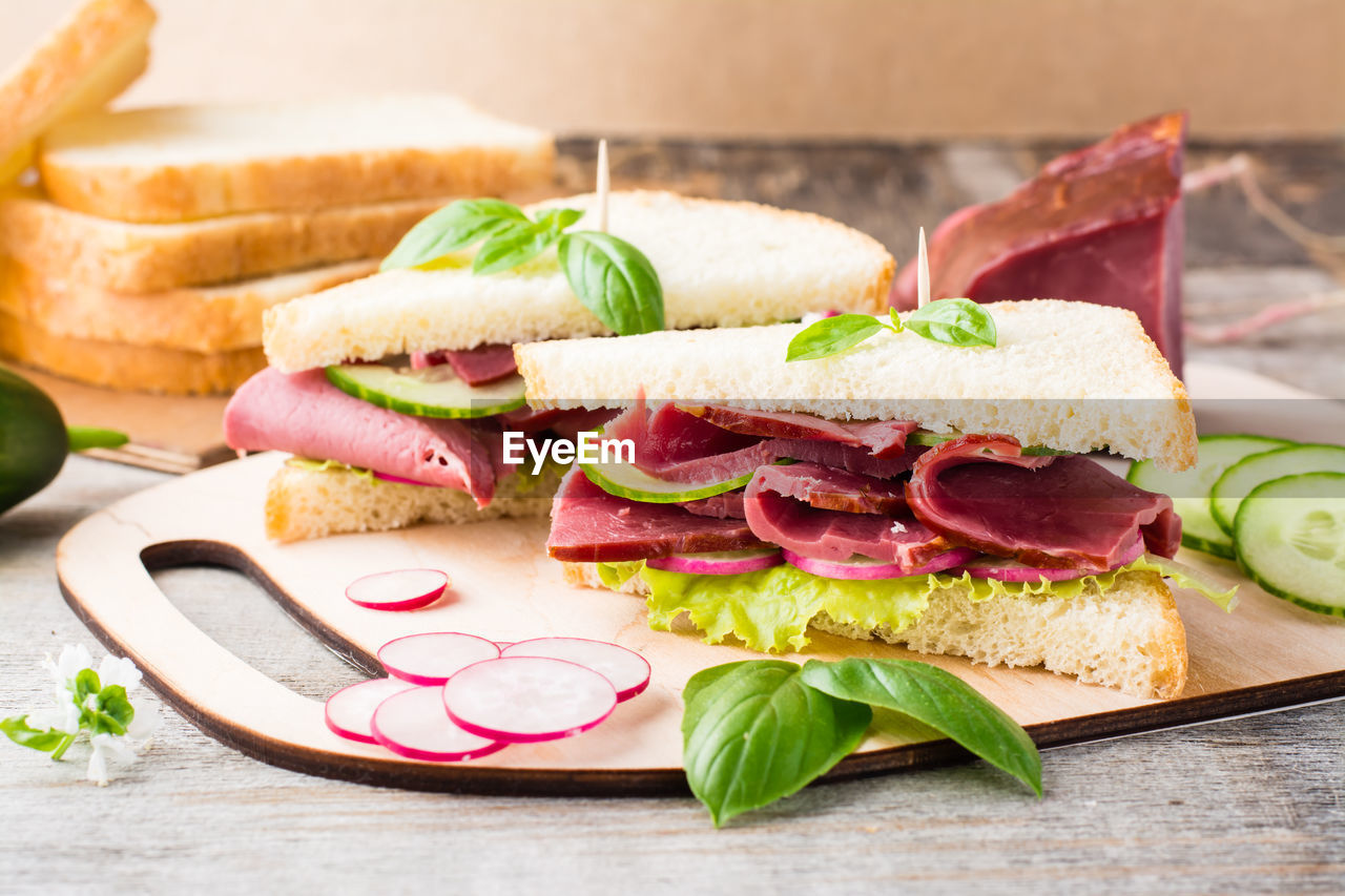 Fresh sandwiches with pastrami and vegetables on a cutting board. american snack. rustic style