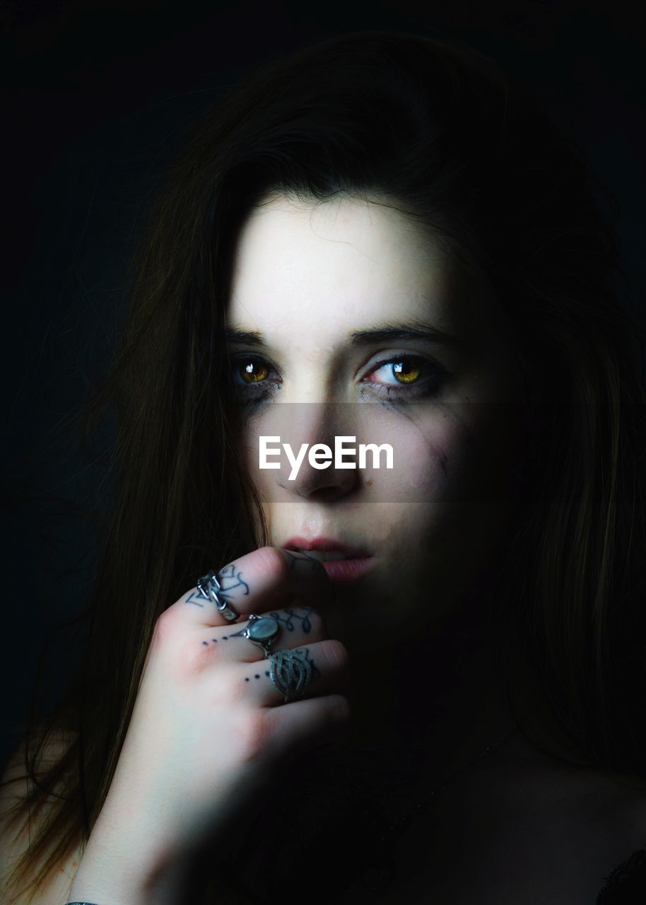 Close-up portrait of young woman against black background