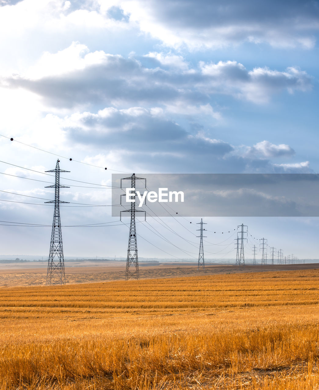 Electricity pylons on field against sky