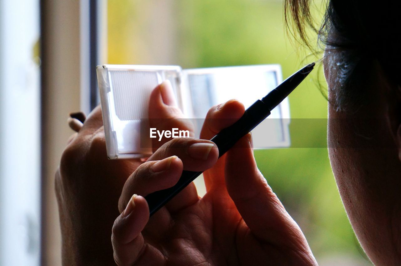 Close-up of woman applying make-up in mirror