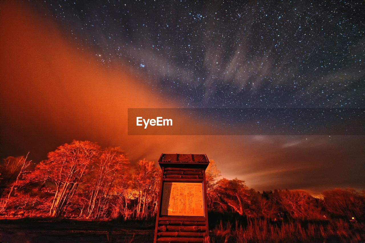 Low angle view of cabin by trees against constellation in sky