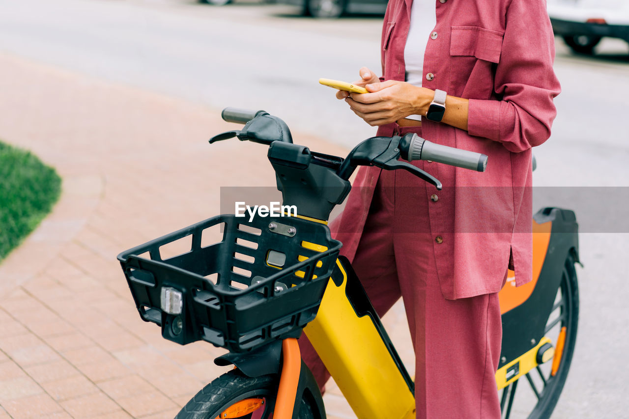 Unrecognizable cropped woman rents an electric city bike using an app on her phone.