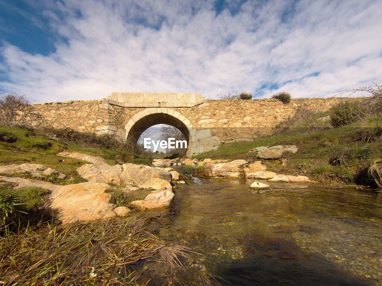 sky, nature, architecture, water, arch, cloud, bridge, built structure, environment, landscape, no people, rock, history, river, travel destinations, scenics - nature, plant, the past, travel, reflection, rural area, outdoors, land, day, tranquility, beauty in nature, ancient, grass, tourism, hill, arch bridge, non-urban scene