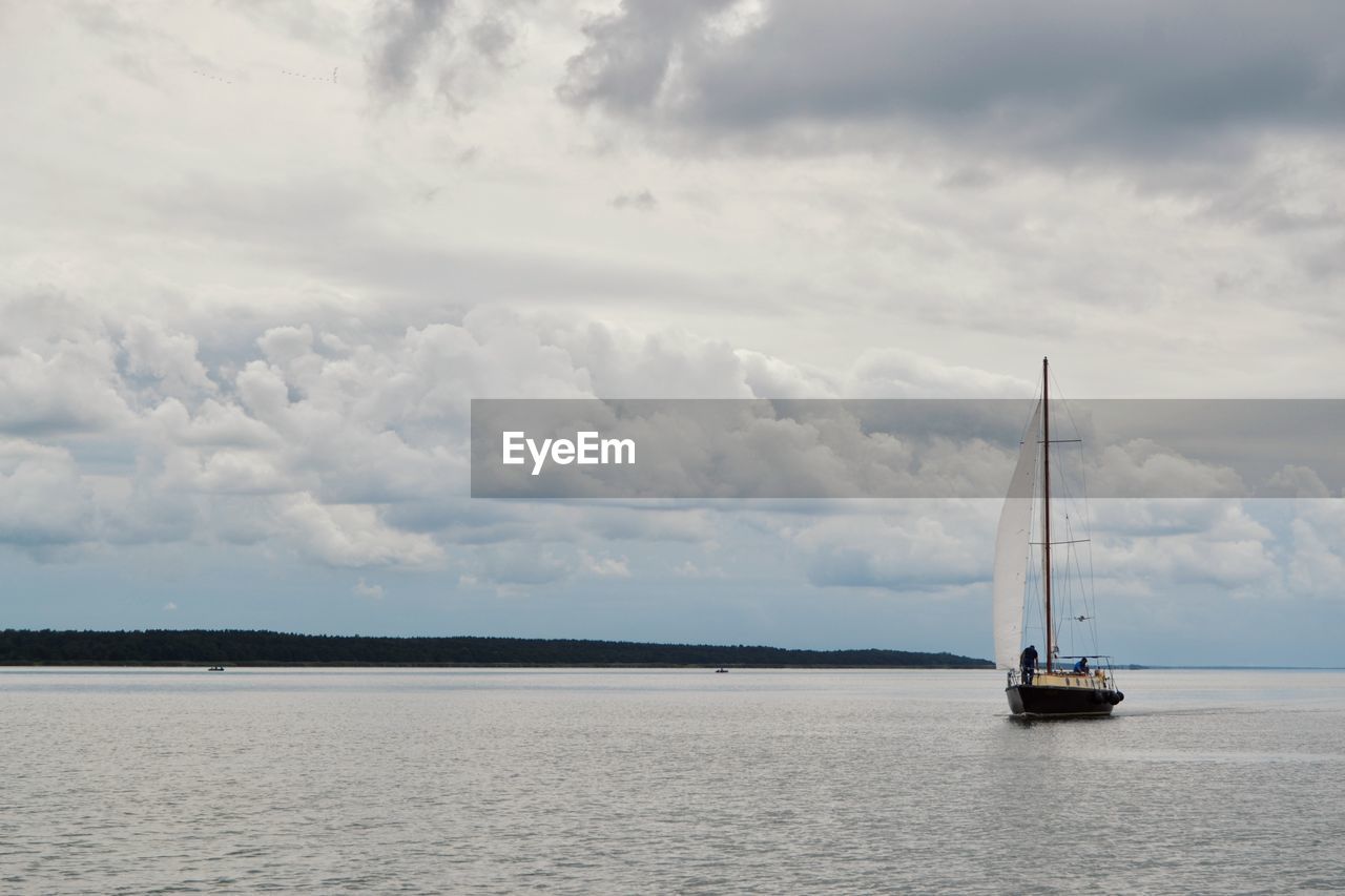 Sailboat sailing on sea against cloudy sky