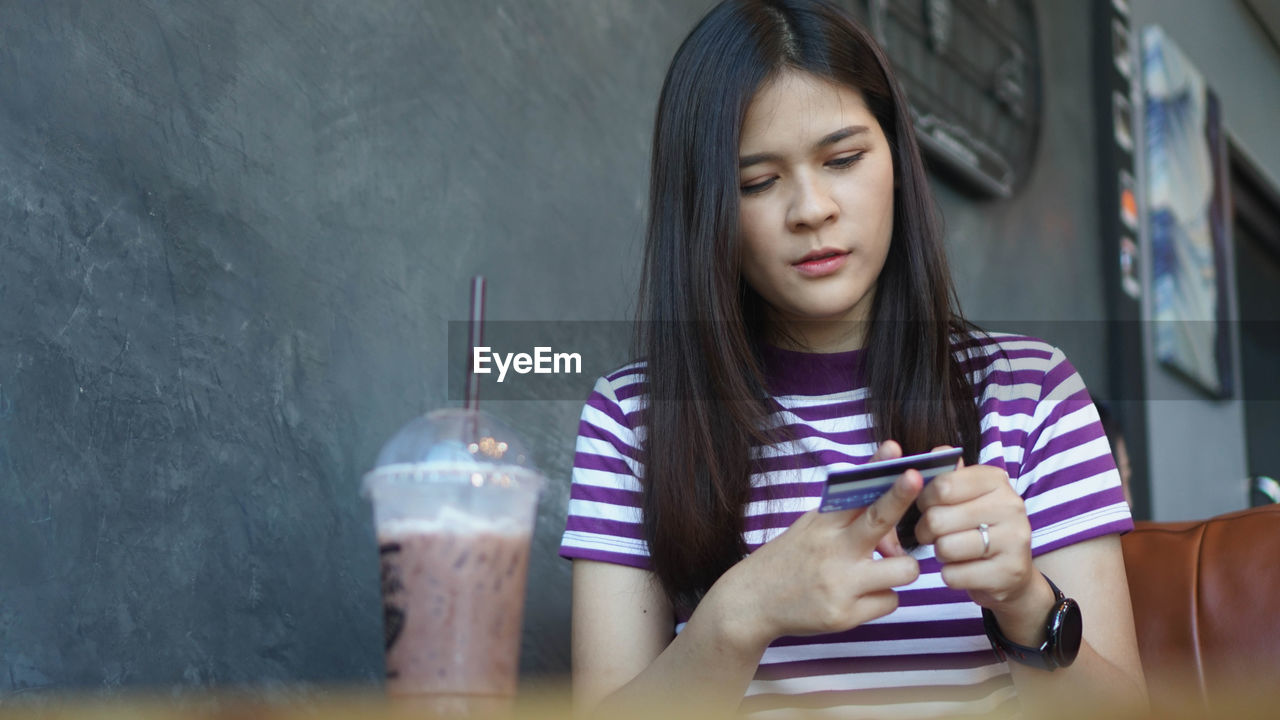 Young woman holding credit card sitting at table with coffee in cafe