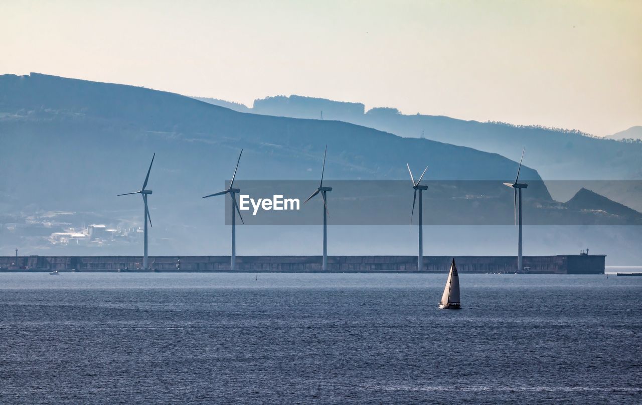 Windmills by sea against mountain