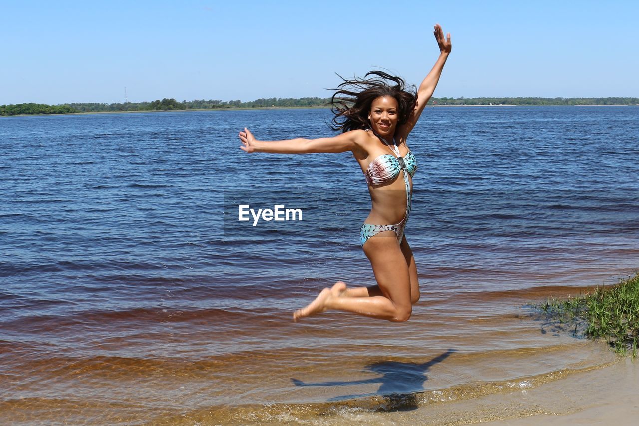 FULL LENGTH OF YOUNG WOMAN JUMPING IN WATER
