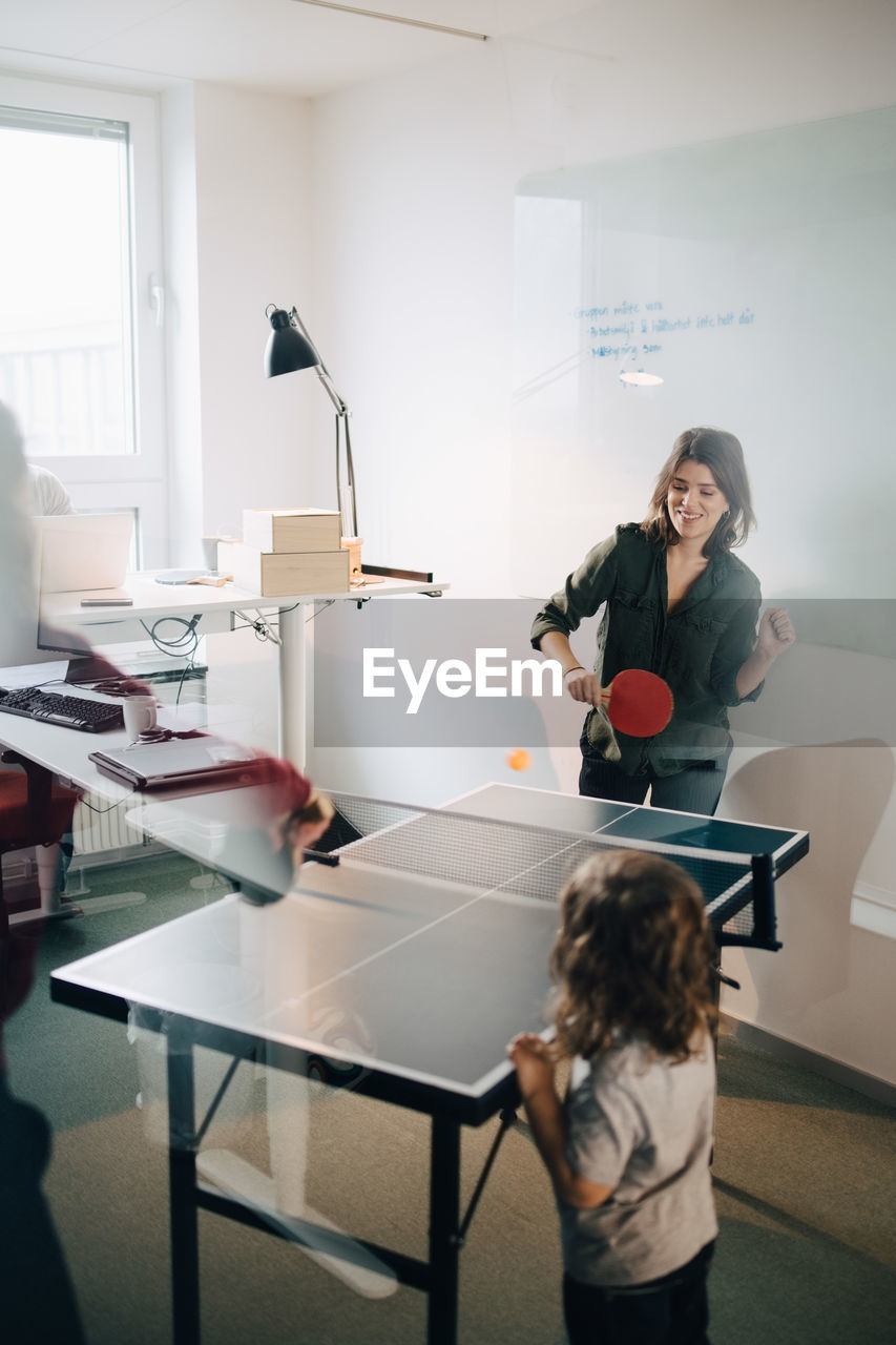 Boy looking at female professionals playing table tennis in creative office