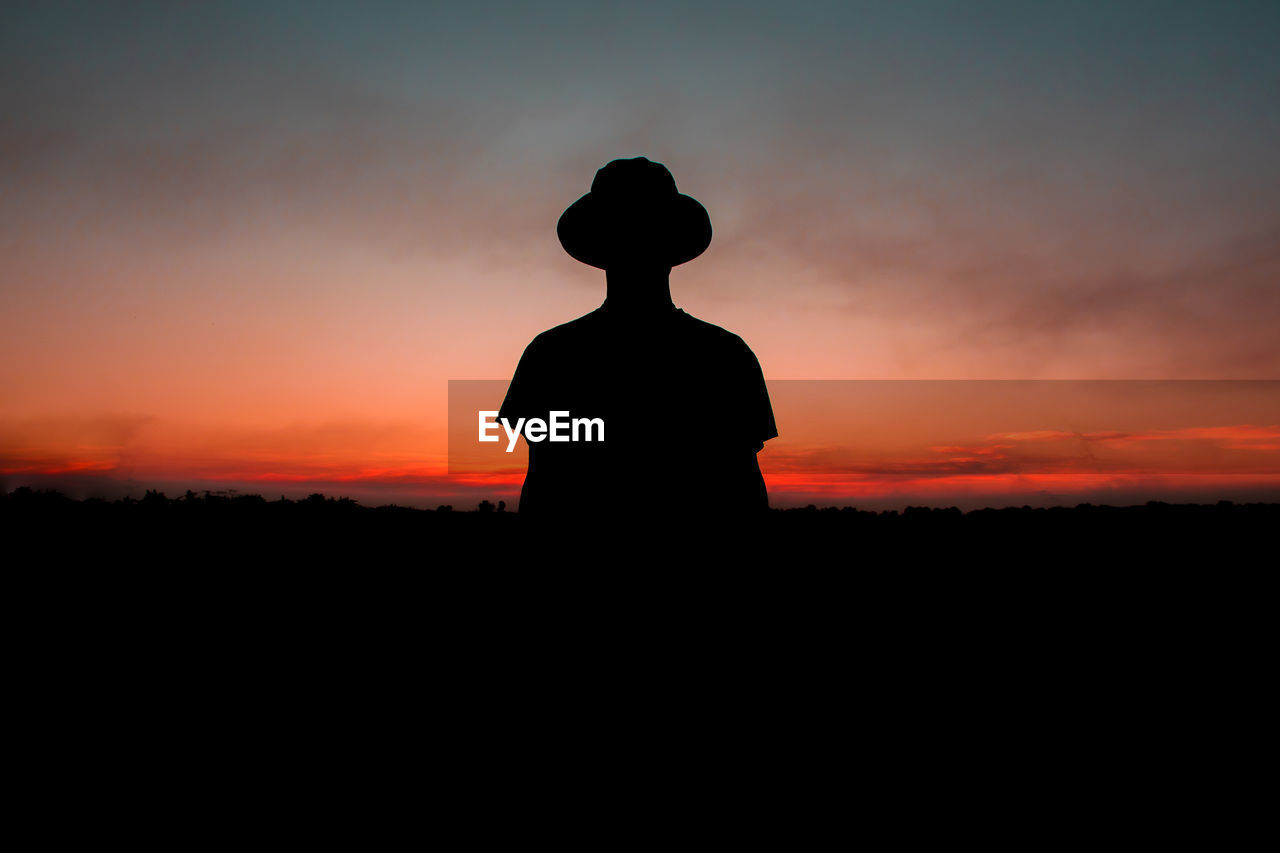 Silhouette man standing on field against sky during sunset