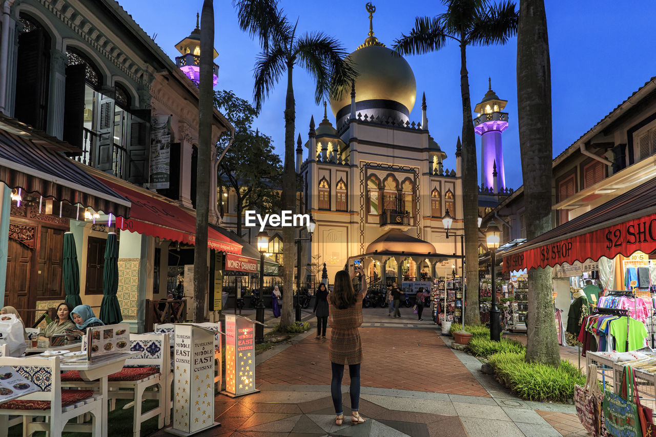 PEOPLE WALKING ON STREET AMIDST BUILDINGS AT NIGHT