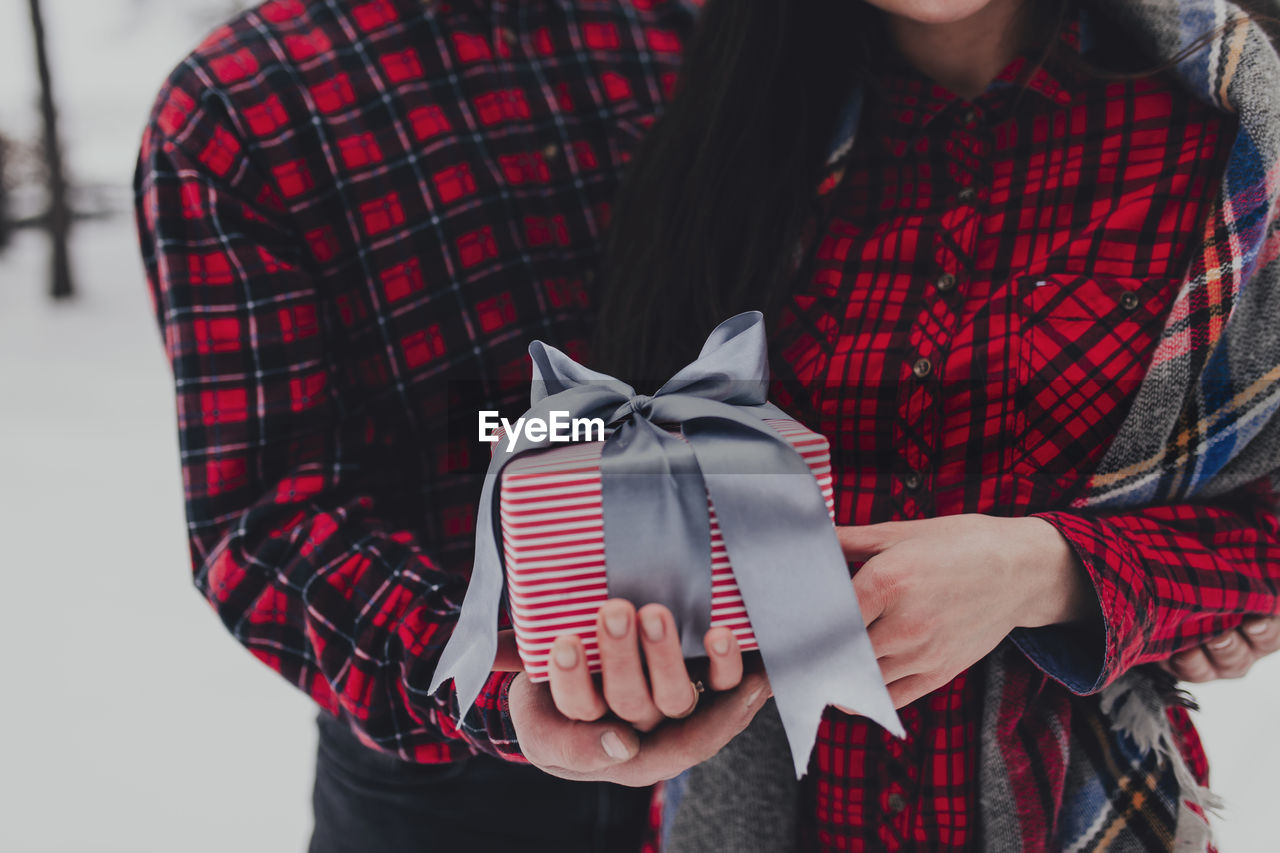 pattern, tartan, red, plaid, clothing, adult, holding, midsection, women, gift, emotion, winter, checked pattern, young adult, one person, textile, front view, casual clothing, fashion, christmas, standing, bow, celebration, positive emotion, tied bow, spring, indoors, love, hand, person, maroon, female, lifestyles, focus on foreground