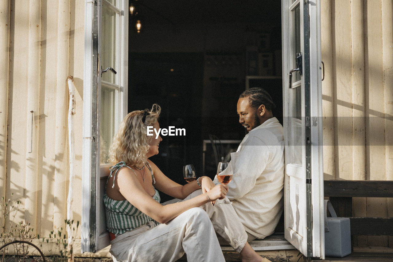 Man and woman enjoying wine while talking to each other sitting at cafe doorway