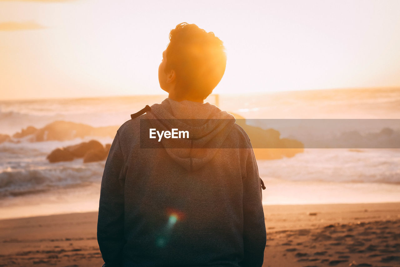 Rear view of man looking at sea against sky during sunset