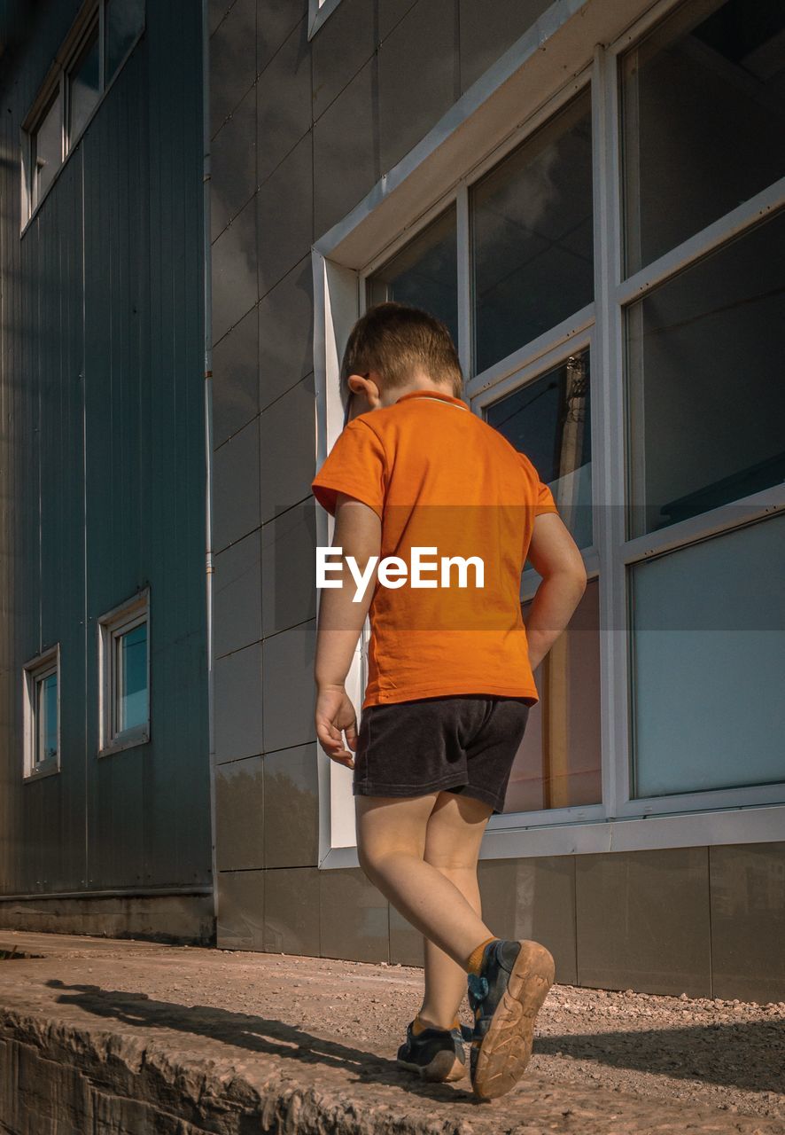 Rear view of boy walking on footpath against building