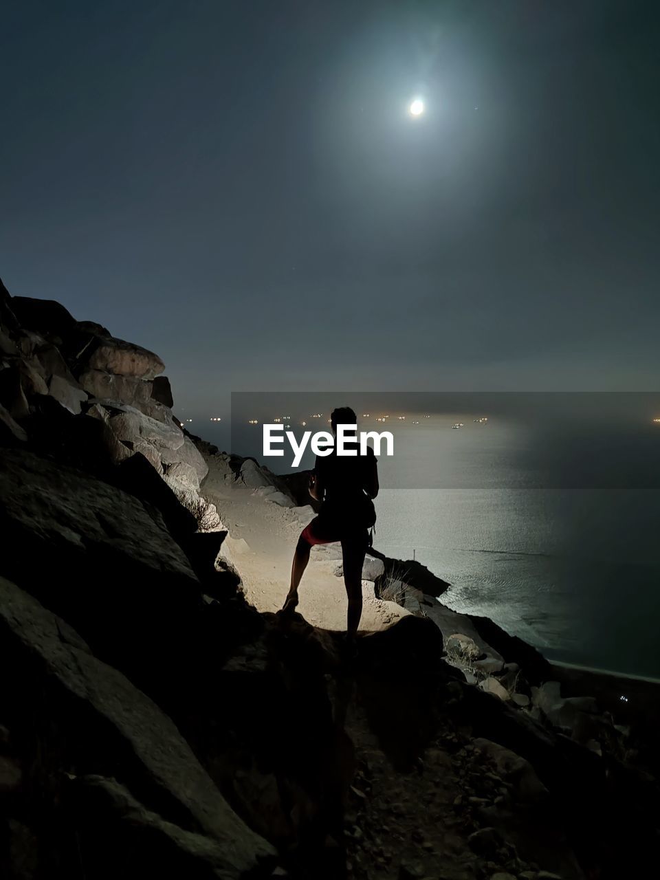 Woman standing on rock by sea against sky