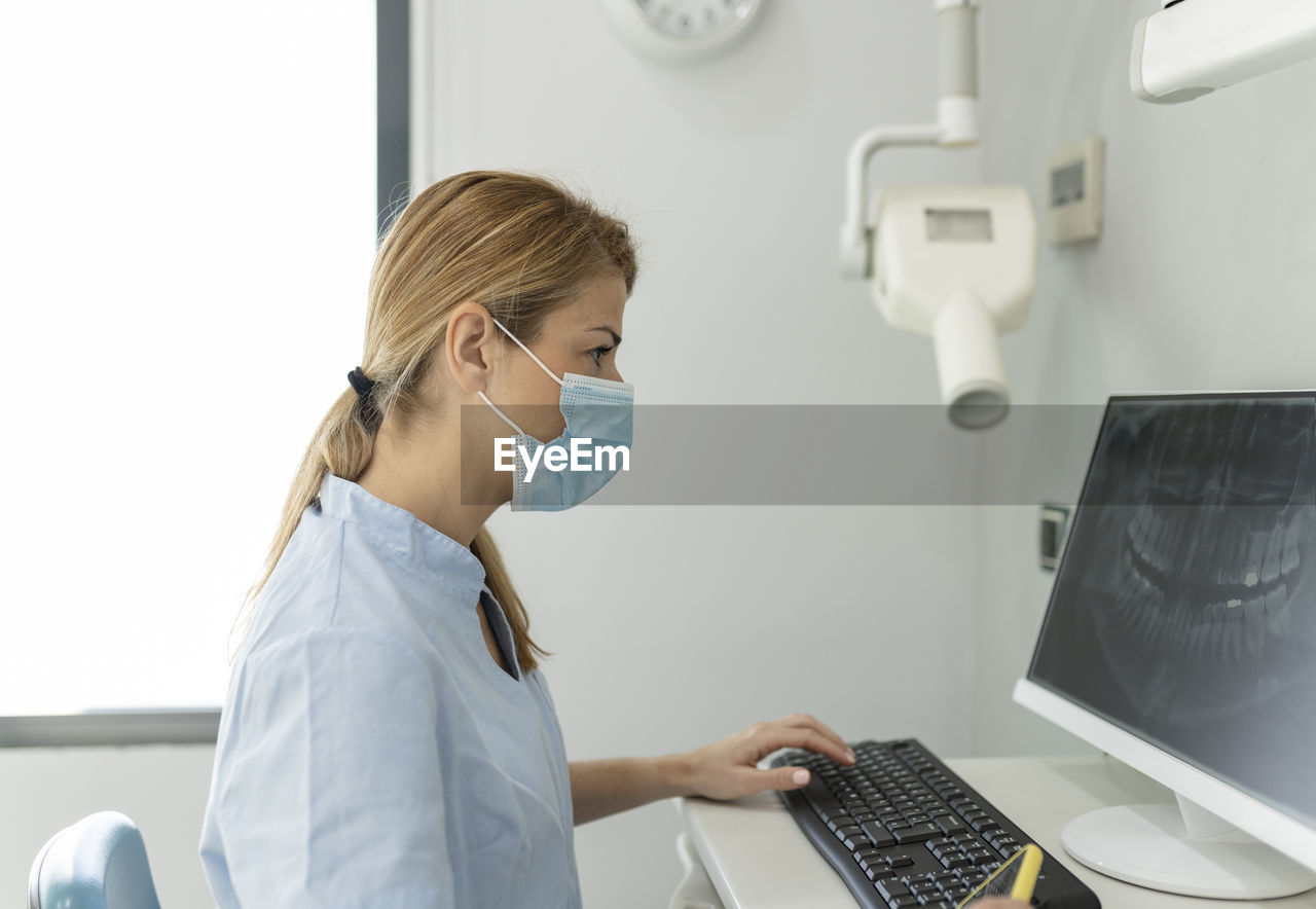 Dentist examining x-ray image through computer at dental clinic