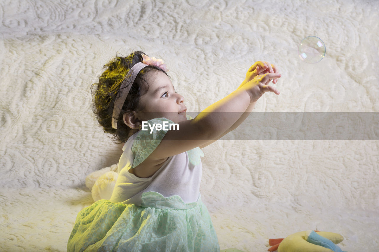 Side view of cute girl trying to catch bubble against wall