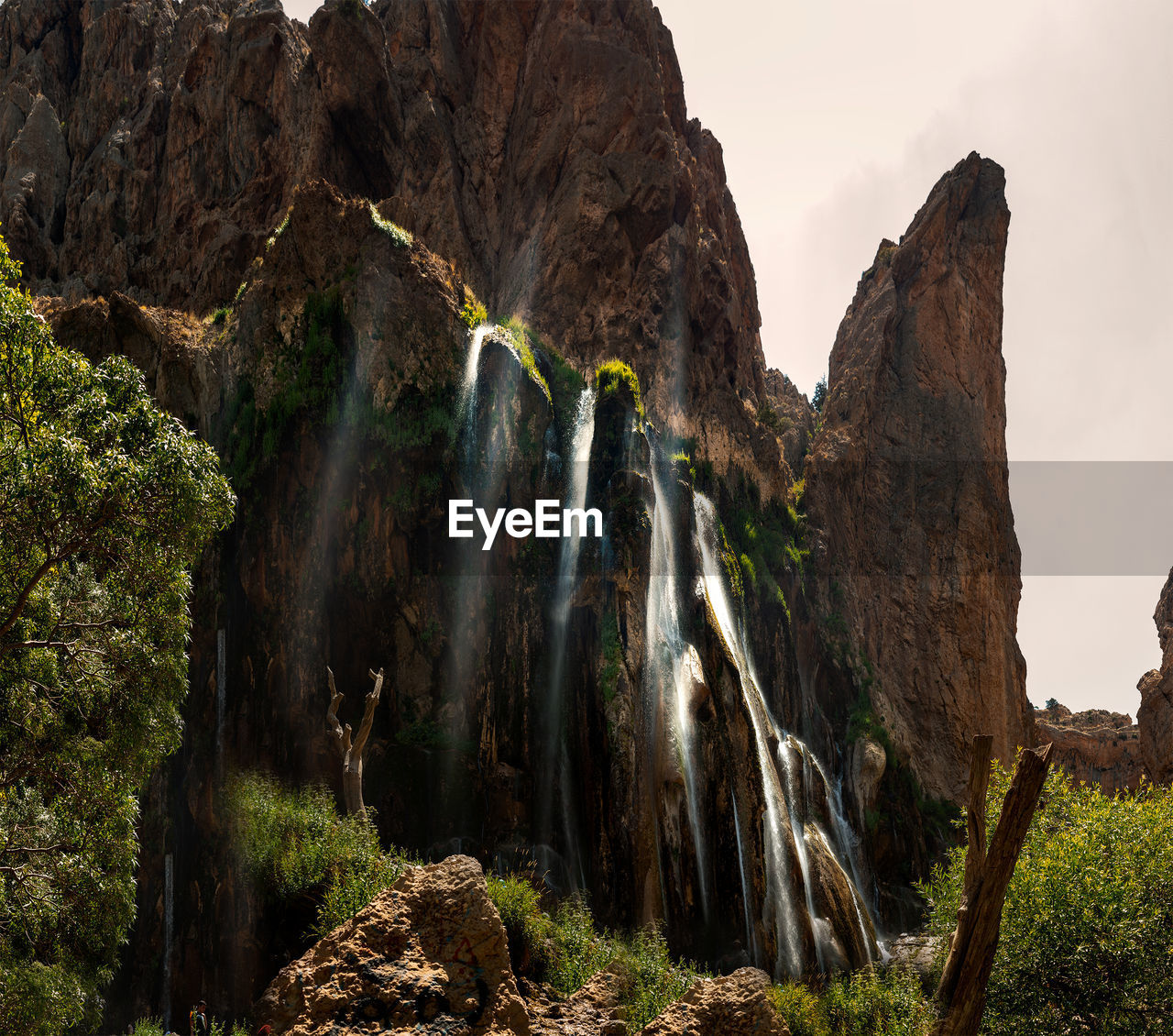 LOW ANGLE VIEW OF WATERFALL AMIDST ROCKS AGAINST SKY