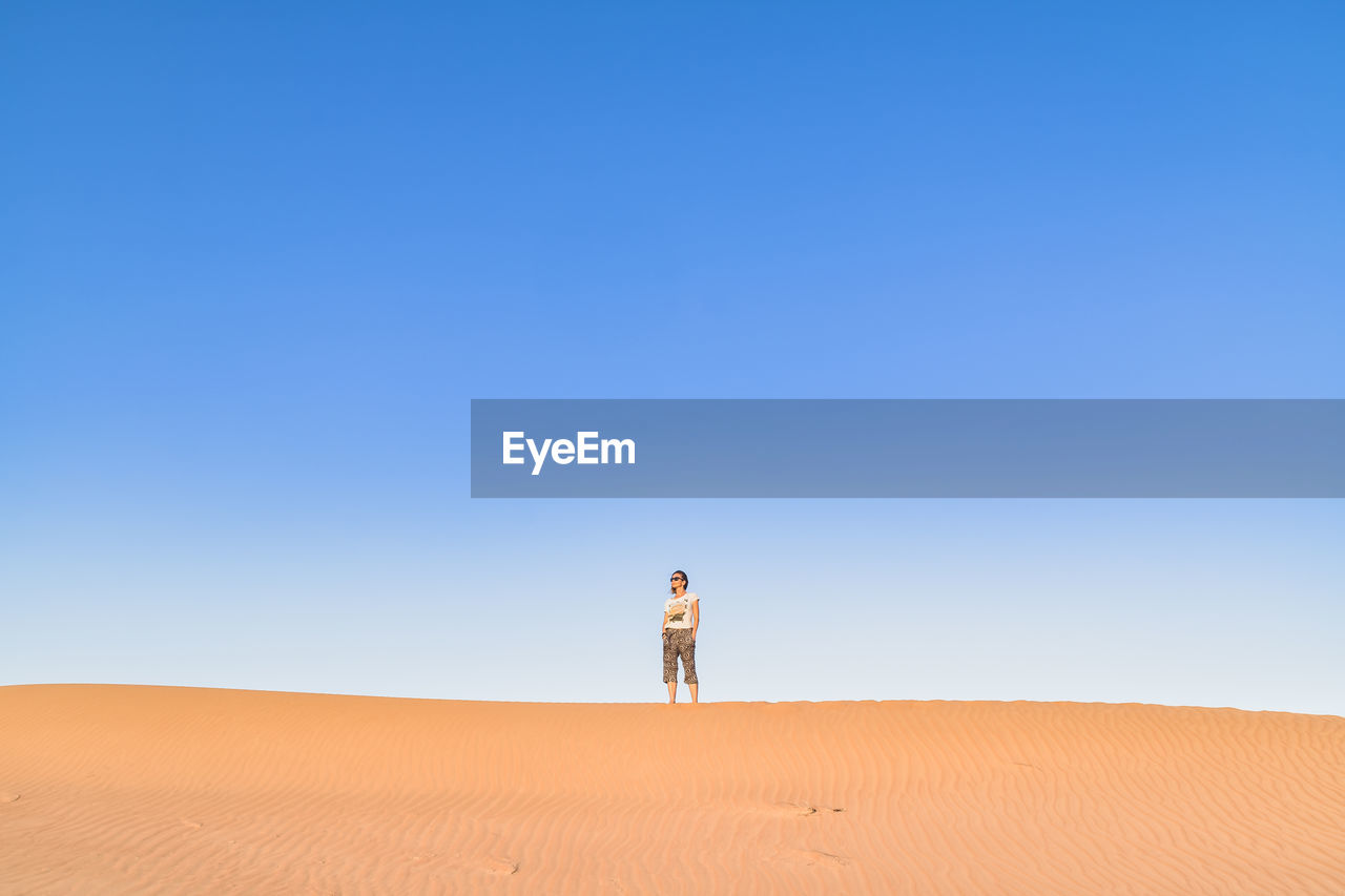 Woman standing on desert against clear blue sky