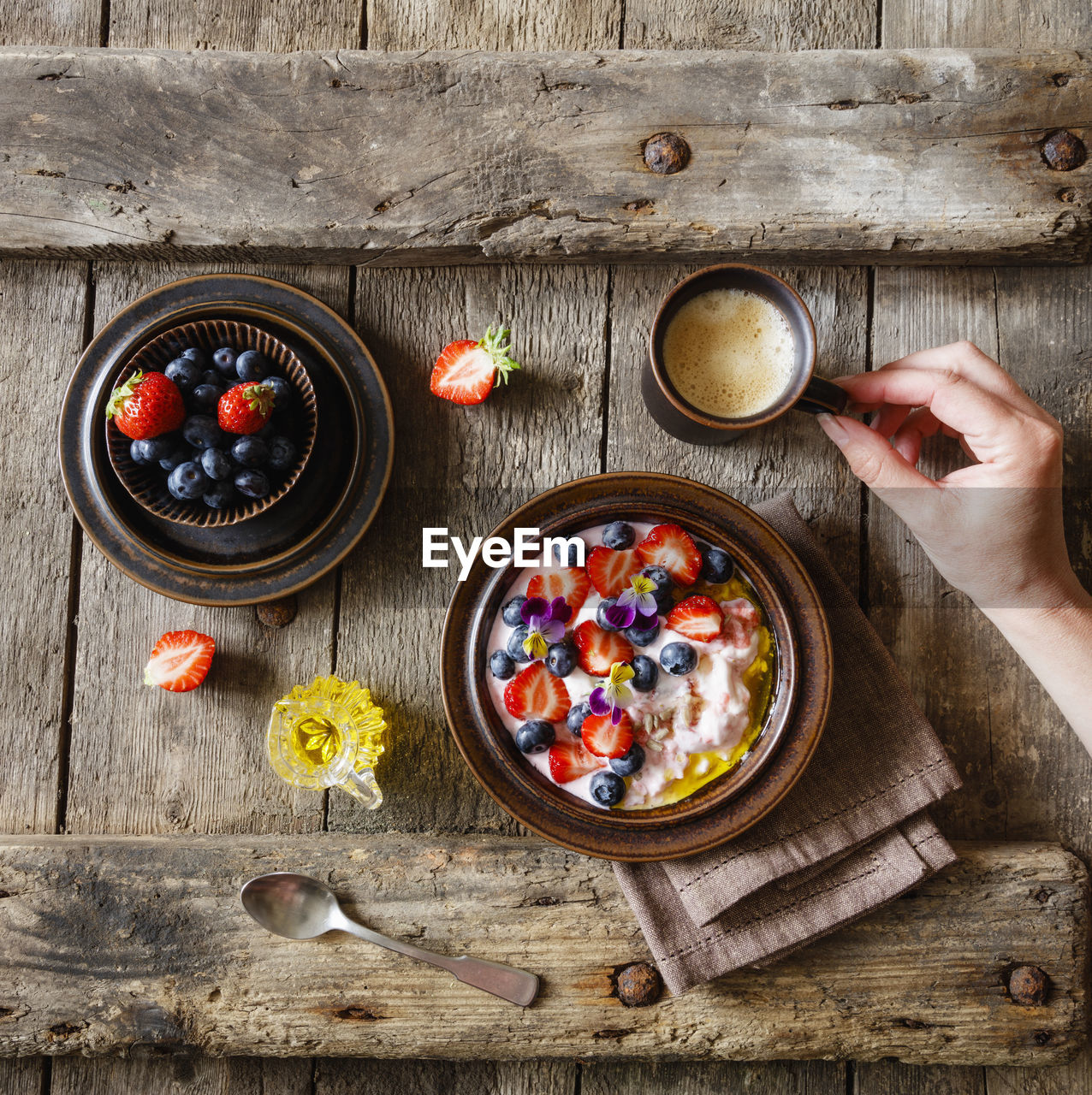 Female hand reaching for cup of coffee standing beside plate of quark with fruits and edible flowers