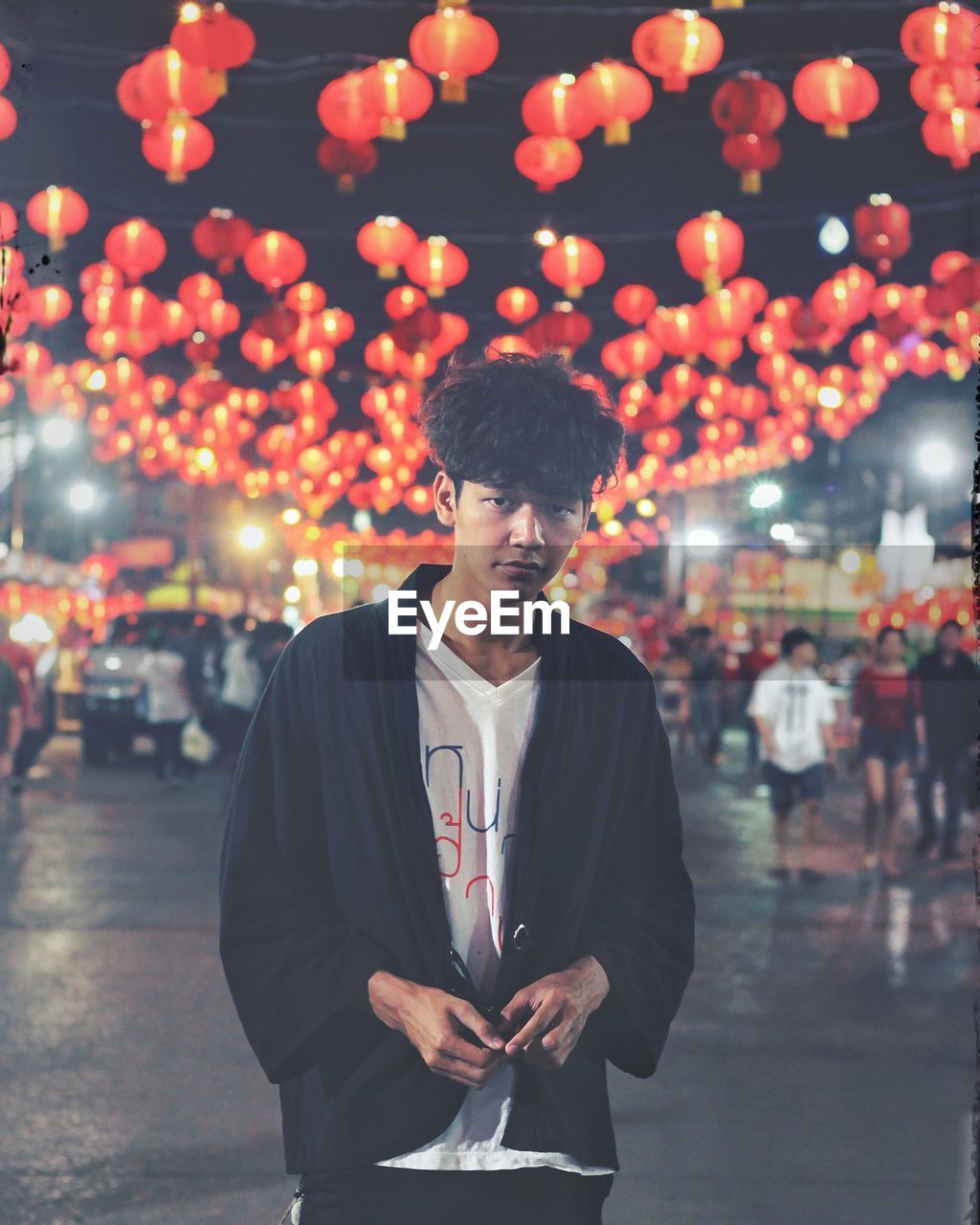 Portrait of young man standing against illuminated lanterns on road at night