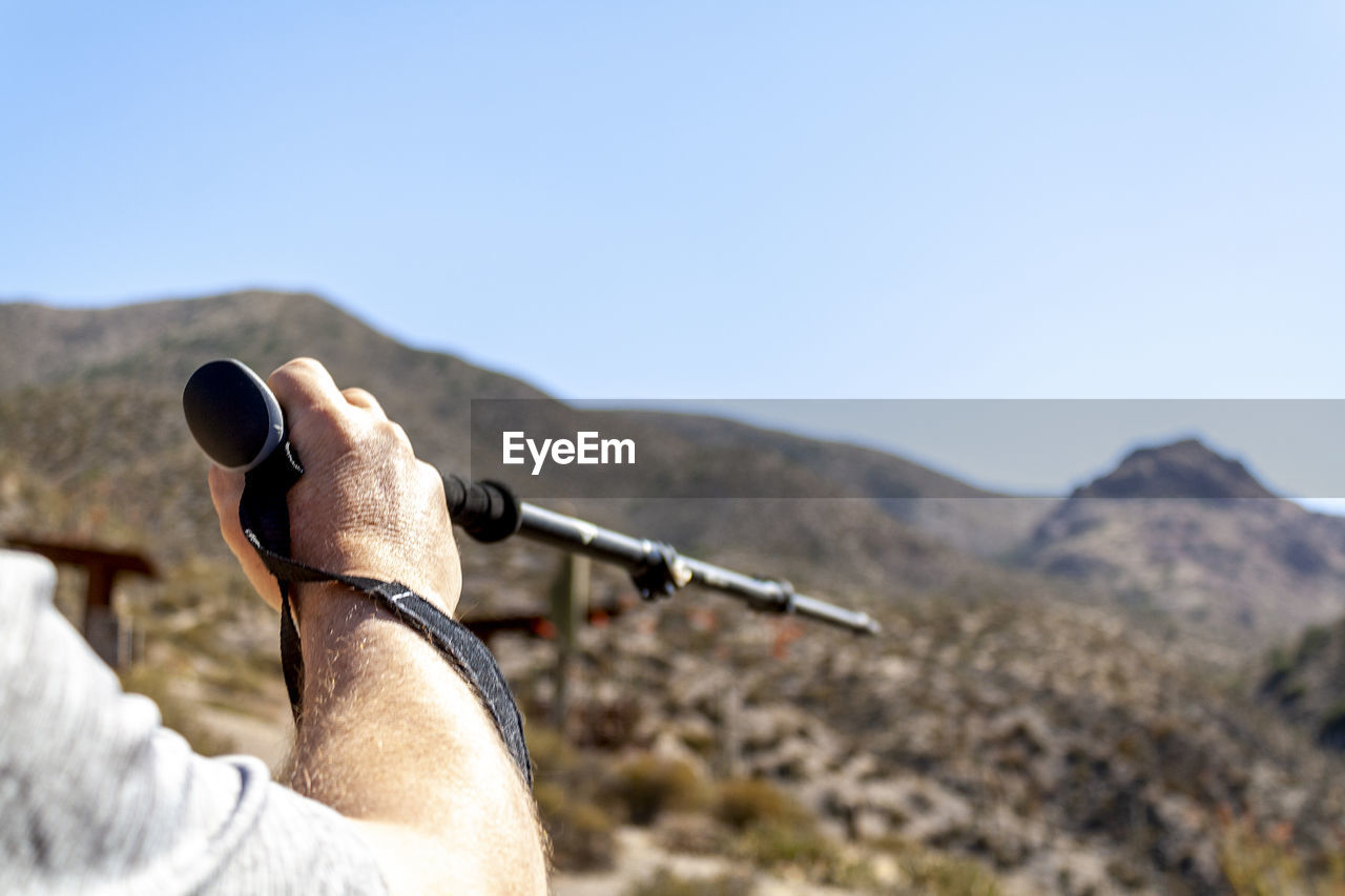 Midsection of man holding hiking pole on mountain against sky