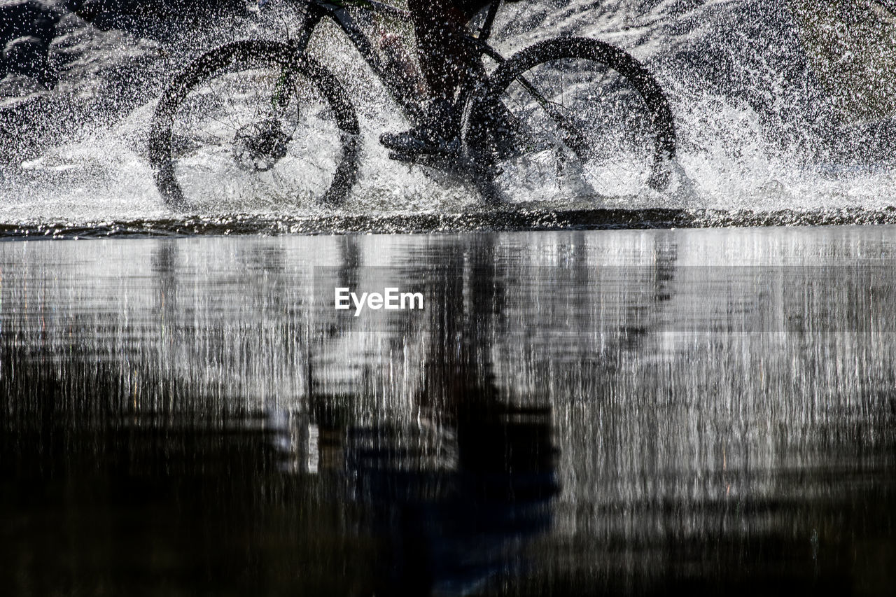 Low section of man riding bicycle in water at shore