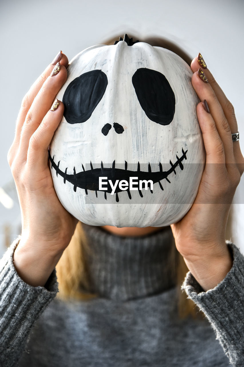 Woman holding funny pumpkin face in front of her face. halloween background diy. do it yourself. 
